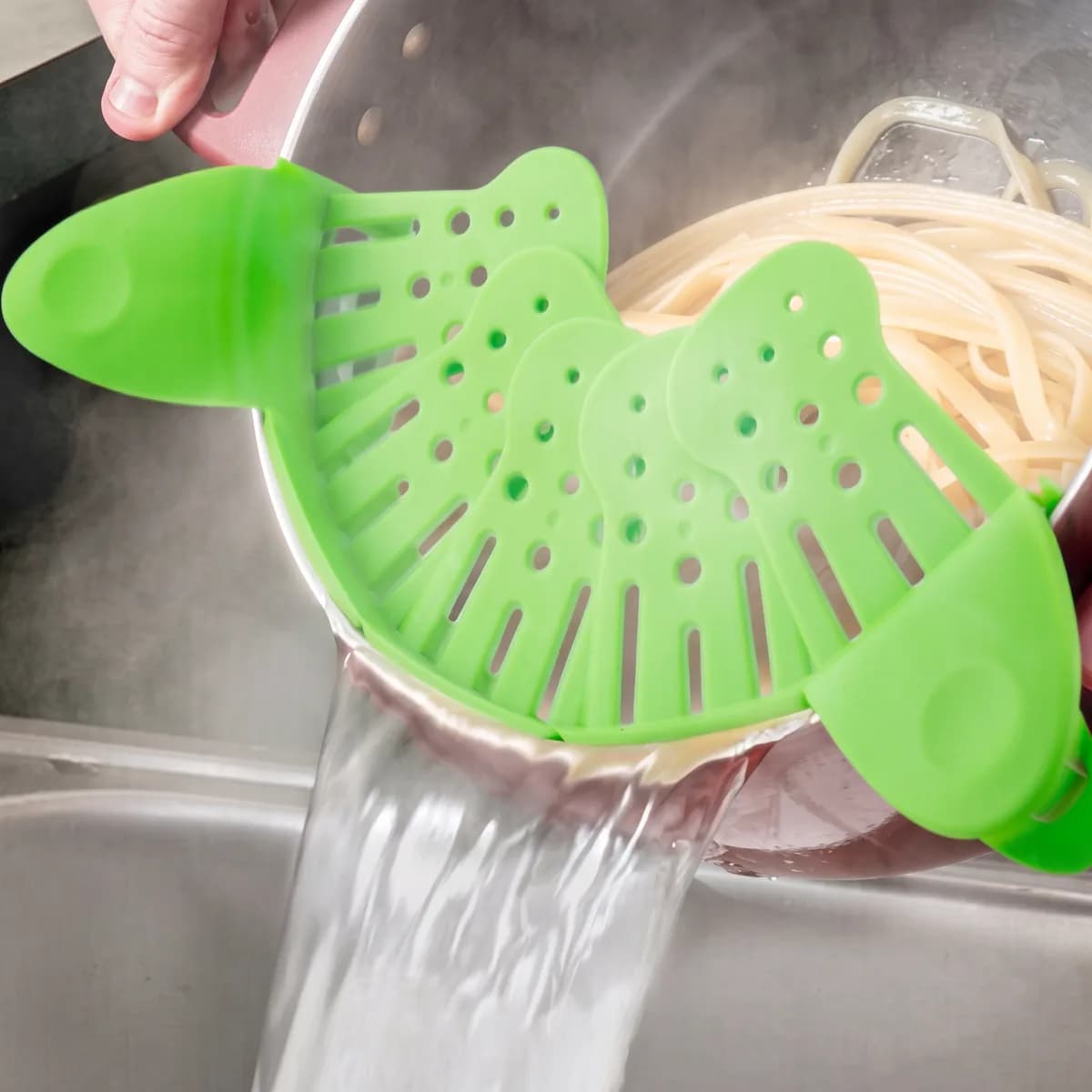 Draining spaghetti over a sink through the green clip-on strainer