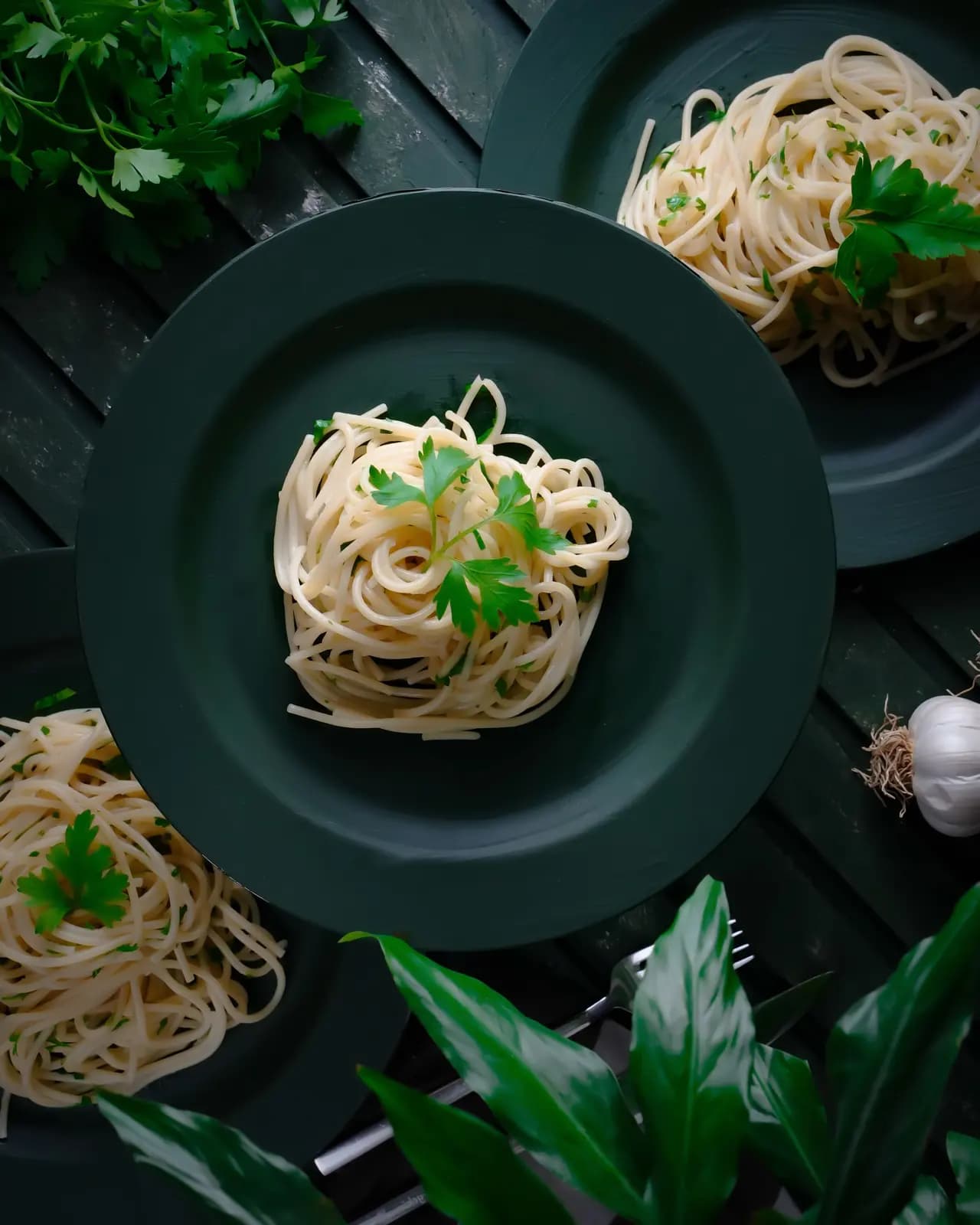 Lemon garlic spaghetti with parsley on a dark green plate