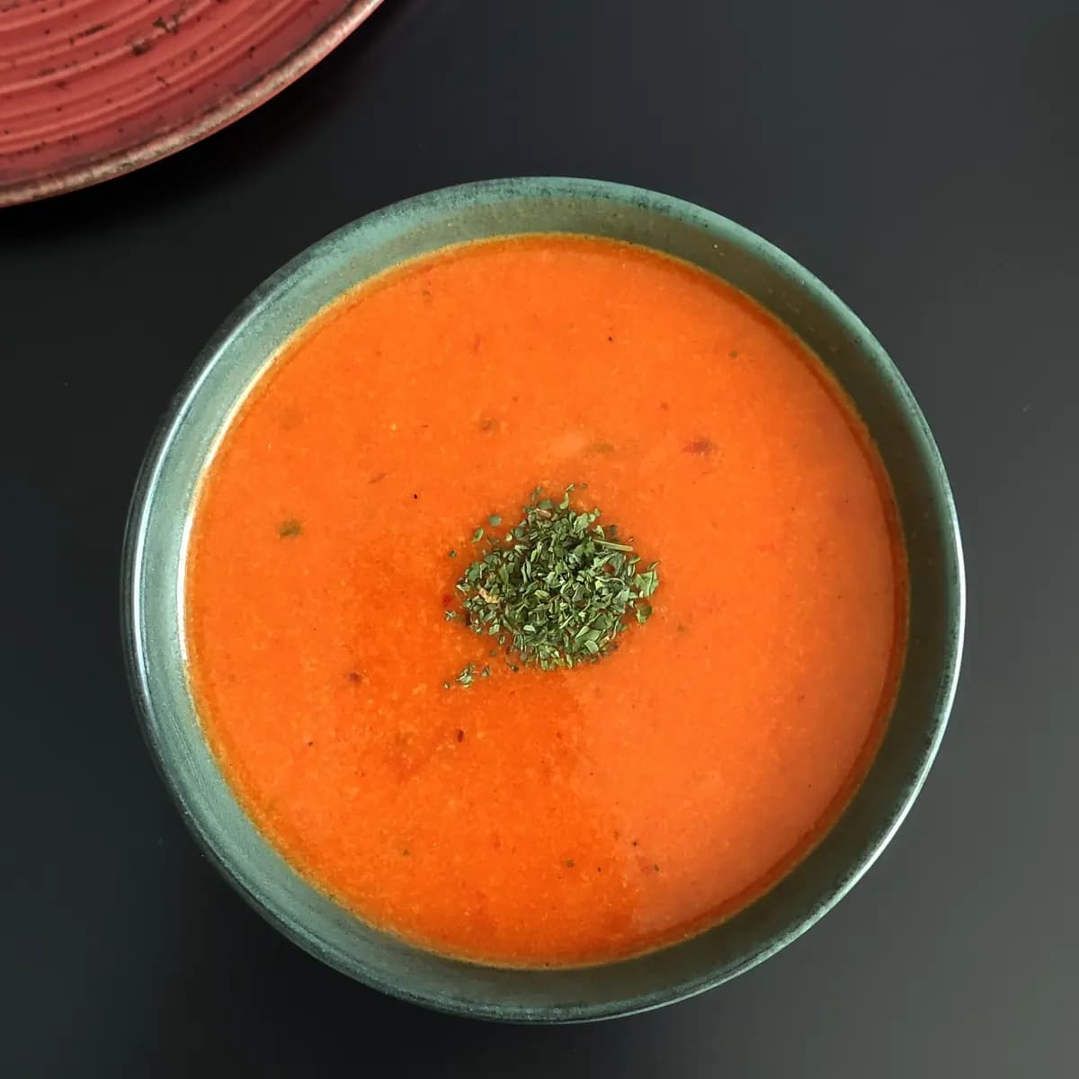 Smooth orange tomato soup topped with chopped parsley in a green bowl