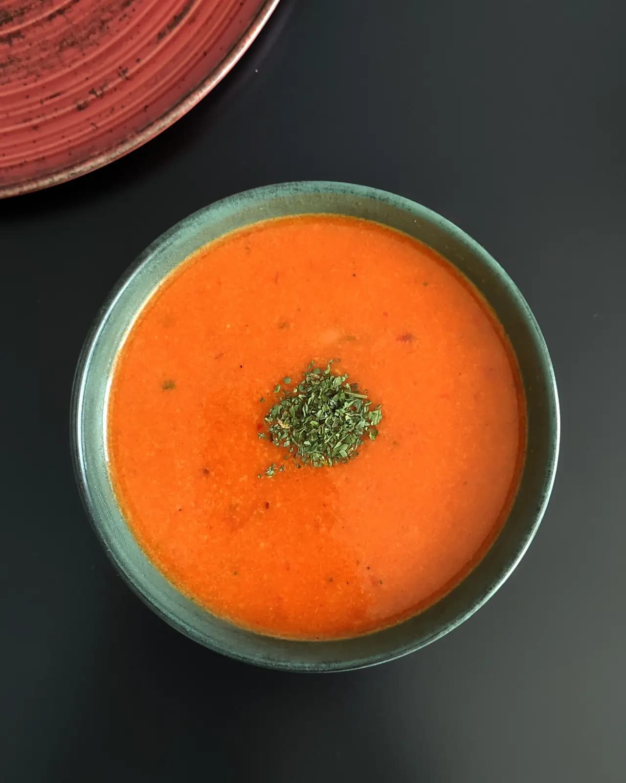 Smooth orange tomato soup topped with chopped parsley in a green bowl