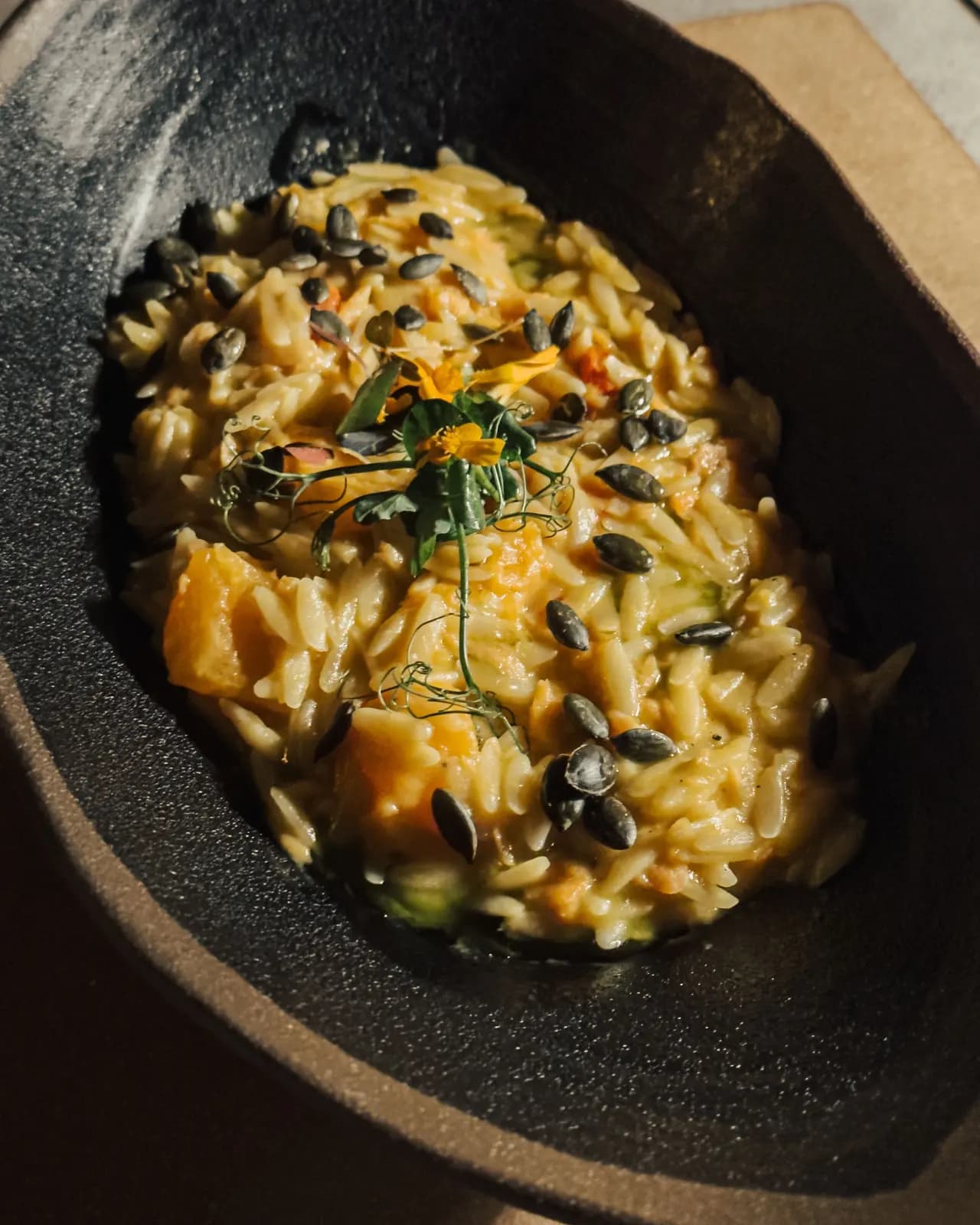 Creamy pumpkin orzo topped with toasted pumpkin seeds and pea shoots in a dark stone bowl