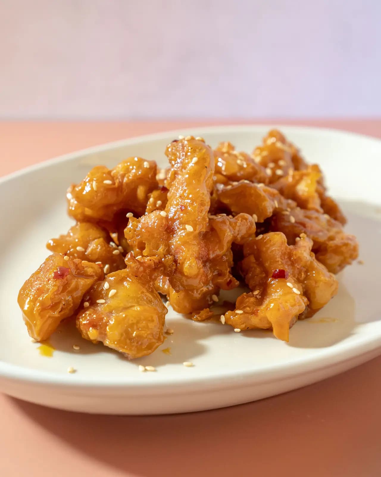 Crispy chicken bites glazed with honey and sprinkled with sesame seeds and red pepper flakes on a white plate