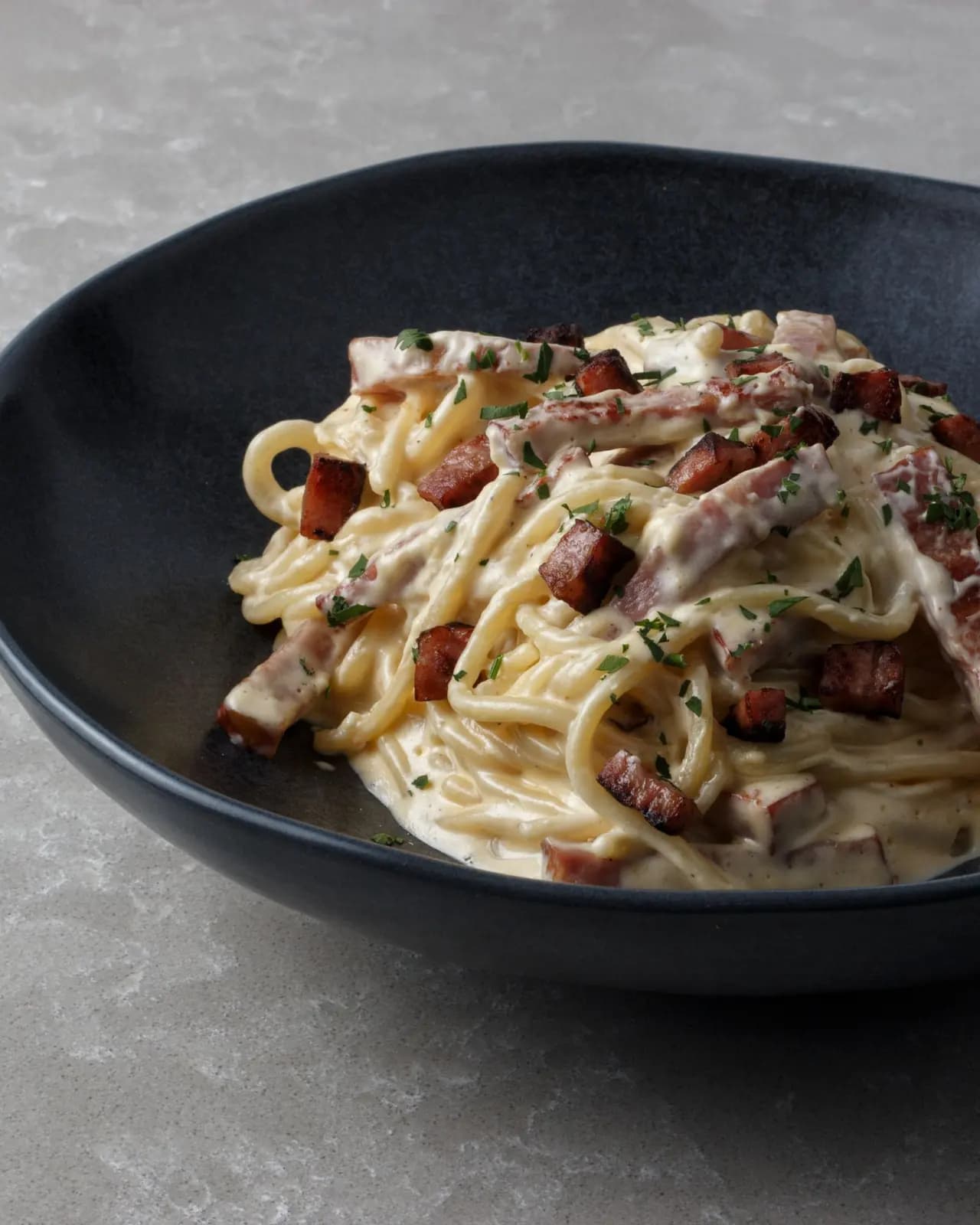 Spaghetti carbonara with strips of crisp pancetta and chopped parsley in a dark blue bowl