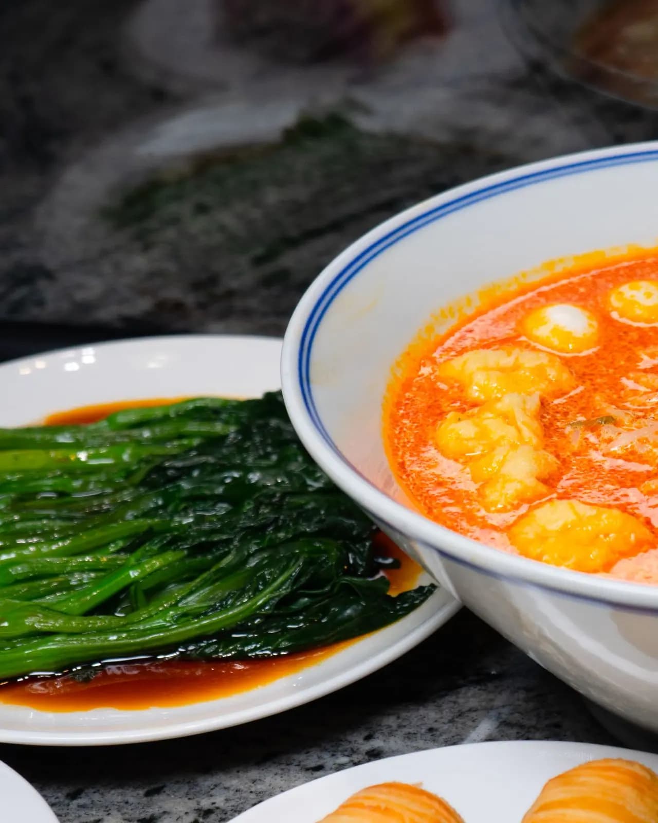 Thai red prawn curry in a blue rimmed white bowl, beside a plate of glossy steamed greens